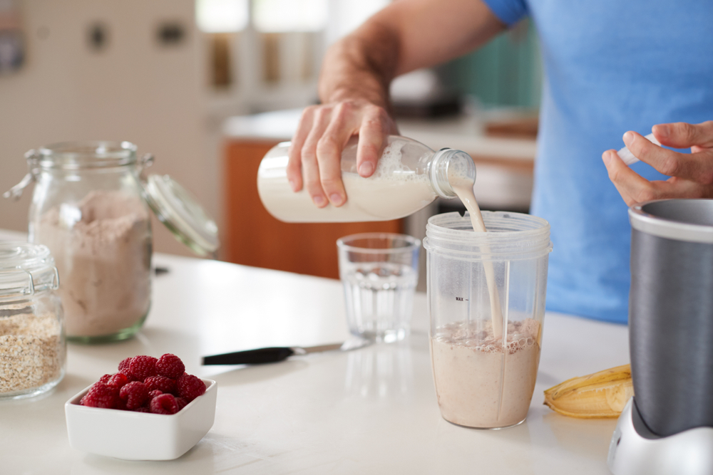 "Image of a fit man making a protein shake with a blender bottle and whey protein powder.